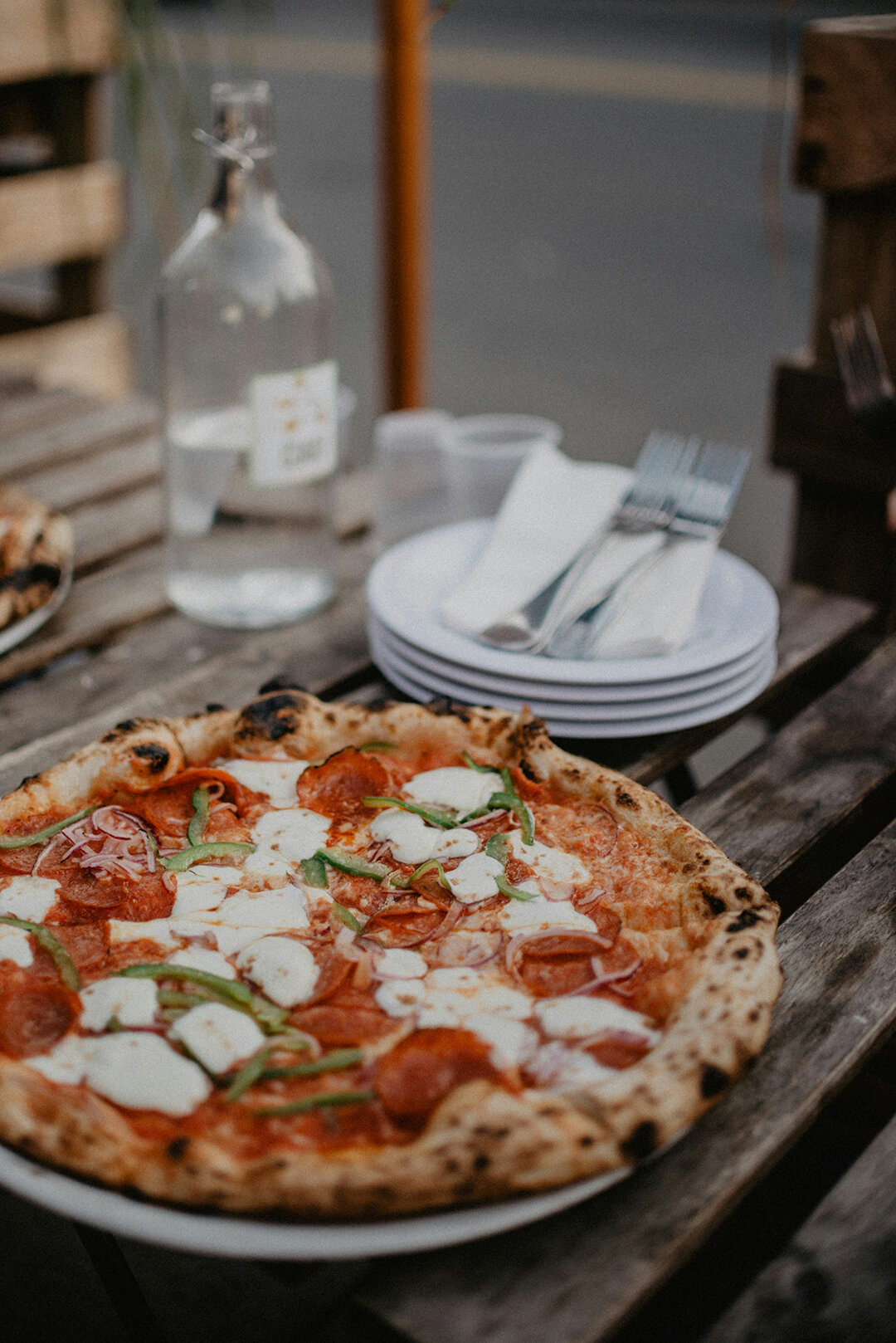 Pizza mit Salami und Mozzarella und ein Stapel Teller mit Gabeln daneben